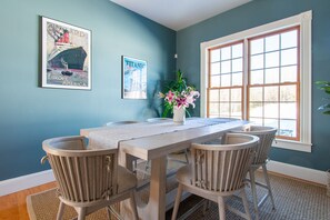 Un comedor con una mesa de madera, cuatro sillas, un jarrón con flores y dos carteles enmarcados en la pared.