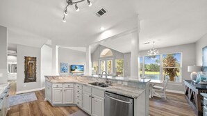 A spacious kitchen with a large island, white cabinetry, and a view of the outdoors.