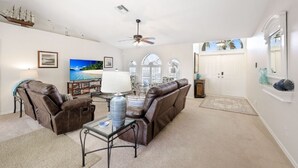 Ein Wohnzimmer mit braunem Ledersofa, einem Glastisch, einem Fernseher und einem Deckenventilator.