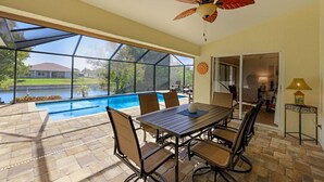 Ein Wintergarten mit Blick auf einen Swimmingpool, einem Deckenventilator und einem Esstisch mit Stühlen.