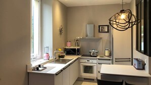 A compact kitchen with a window, a sink, a stove, and a dining area with two chairs.