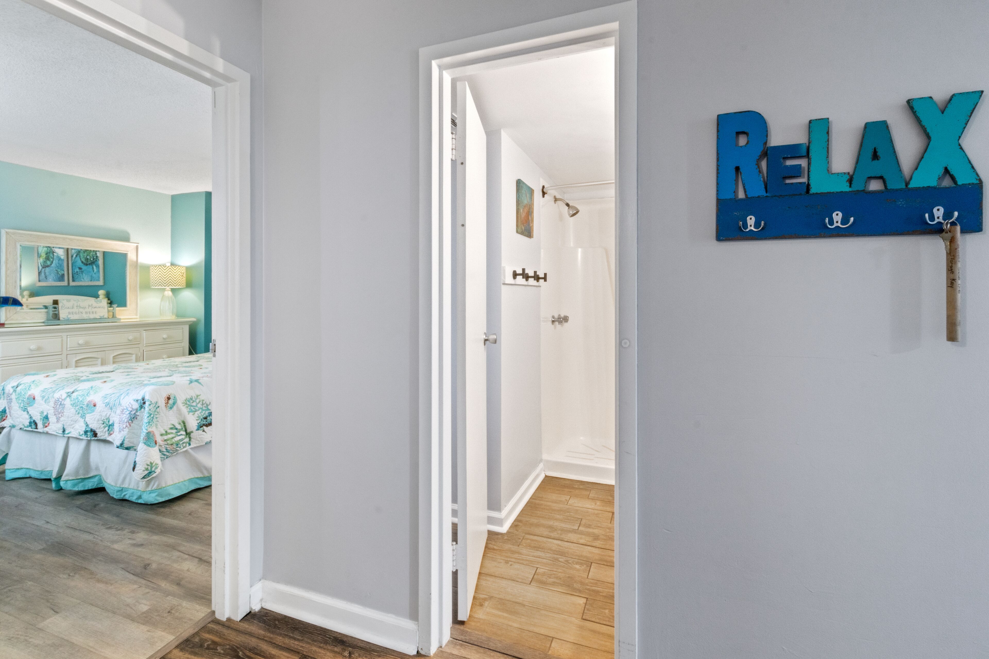 A hallway with a 'RELAX' sign, a bathroom with a shower, and a bedroom with a bed and a nightstand.