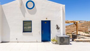 A white building with a blue door and window, a circular blue sign above the door, and a stone wall in the background.