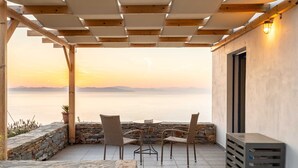 A covered outdoor seating area with stone walls, a view of the sea, and a pergola structure.