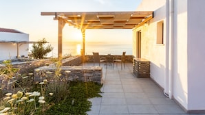 En terrasse med pergola, stenbænke og udsigt til solnedgangen over vandet.