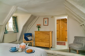 A cozy attic bedroom with a bed, a dresser, a chair, and a door leading to another room. - Finest Retreats | The West Wing at Gypsy Hall (Dullingham)