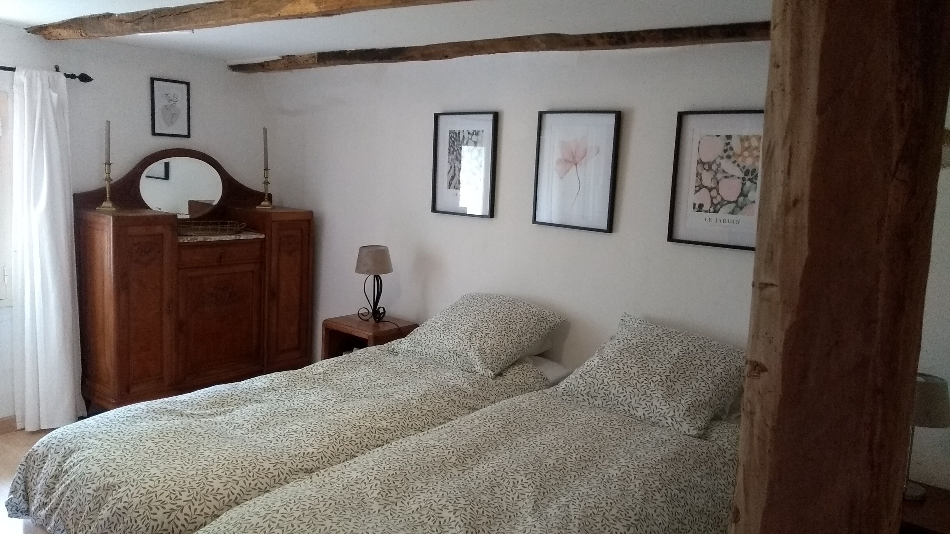 Une chambre à coucher avec un lit, une commode en bois, une table de chevet avec une lampe et des tableaux encadrés accrochés au mur.