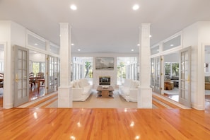 A spacious living room with a fireplace, white furniture, and large windows.