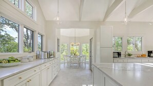 A spacious kitchen with white cabinetry, a marble countertop, and large windows offering views of greenery. - Sunset Marsh Estate/8BR/Horizon pool/Renovated Gourmet kitchen/sleeps 18 (Kiawah Island)