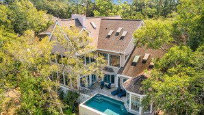 A modern house with a swimming pool, large windows, and a covered patio area surrounded by trees. - Sunset Marsh Estate/8BR/Horizon pool/Renovated Gourmet kitchen/sleeps 18 (Kiawah Island)