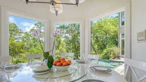 A dining area with a glass table, white chairs, and a bowl of oranges. - Sunset Marsh Estate/8BR/Horizon pool/Renovated Gourmet kitchen/sleeps 18 (Kiawah Island)