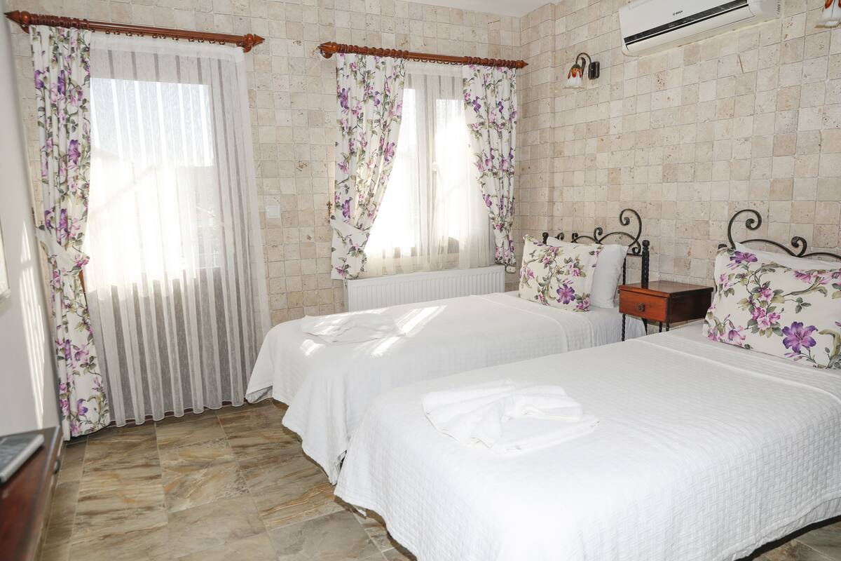 A bedroom with two beds, a radiator, a wooden nightstand, and a wall-mounted air conditioner.