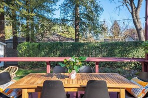 Eine Holzterrasse mit Tisch und Stühlen, umgeben von Grünpflanzen und Bäumen.
