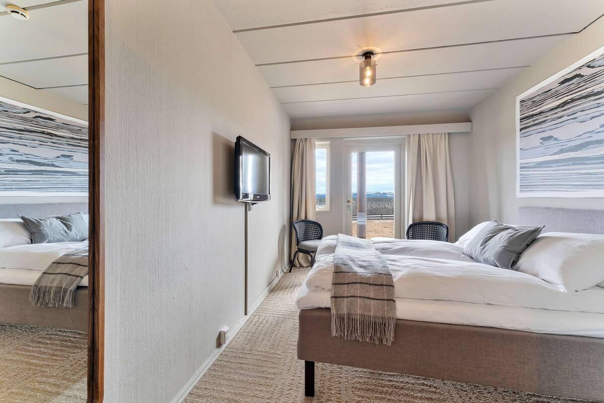 A modern hotel room with a large bed, a flat-screen TV, a view of the outdoors, and a large window with curtains.