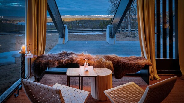 A cozy seating area with a table and chairs, a candle, and a view of a snowy landscape through a large window. - Ranten Hotell, BW Signature Collection (Nes)