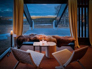 A cozy seating area with a table and chairs, a candle, and a view of a snowy landscape through a large window.