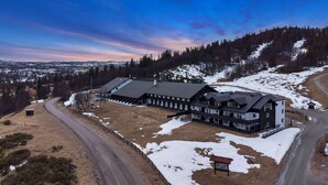 A large, multi-story building with a symmetrical facade, surrounded by snow-covered ground and a forested hillside. - Ranten Hotell, BW Signature Collection (Nes)