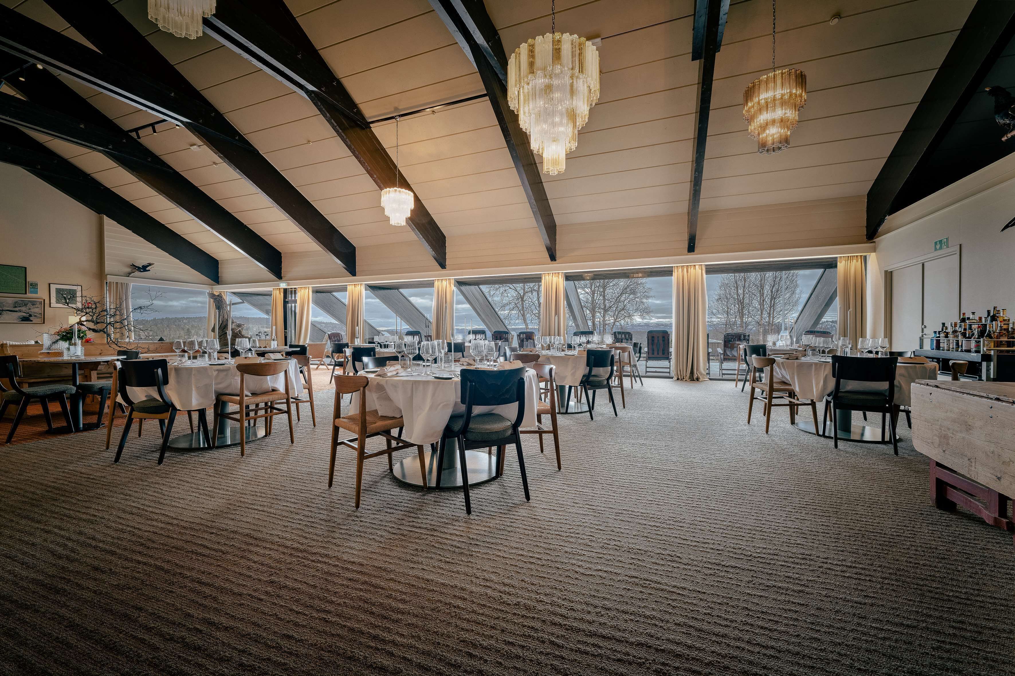 A spacious dining area with multiple tables and chairs, large windows, and chandeliers.