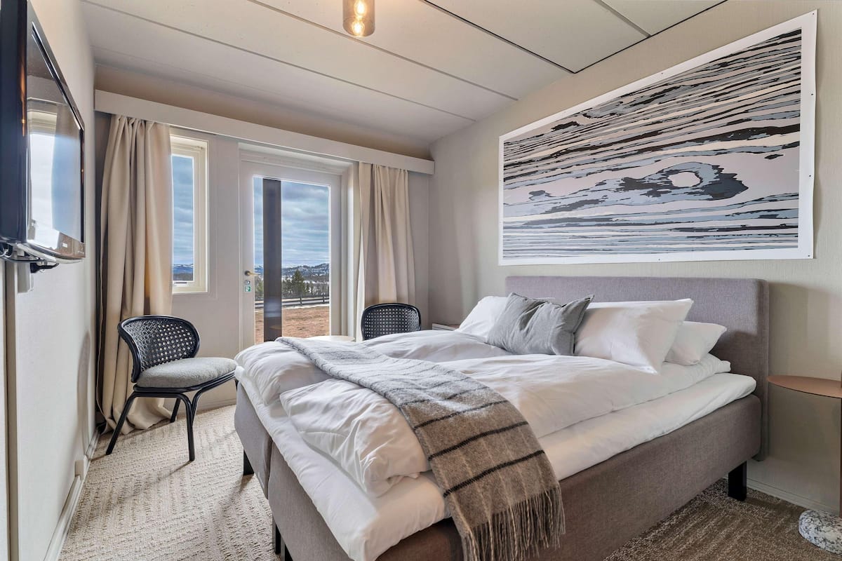 Un dormitorio con una cama, una silla, un televisor y un cuadro abstracto grande en la pared.