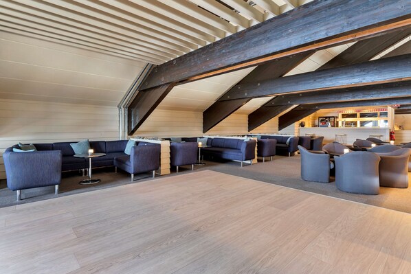 A spacious lounge area with modern seating, a high ceiling with exposed beams, and a view of the bar area.