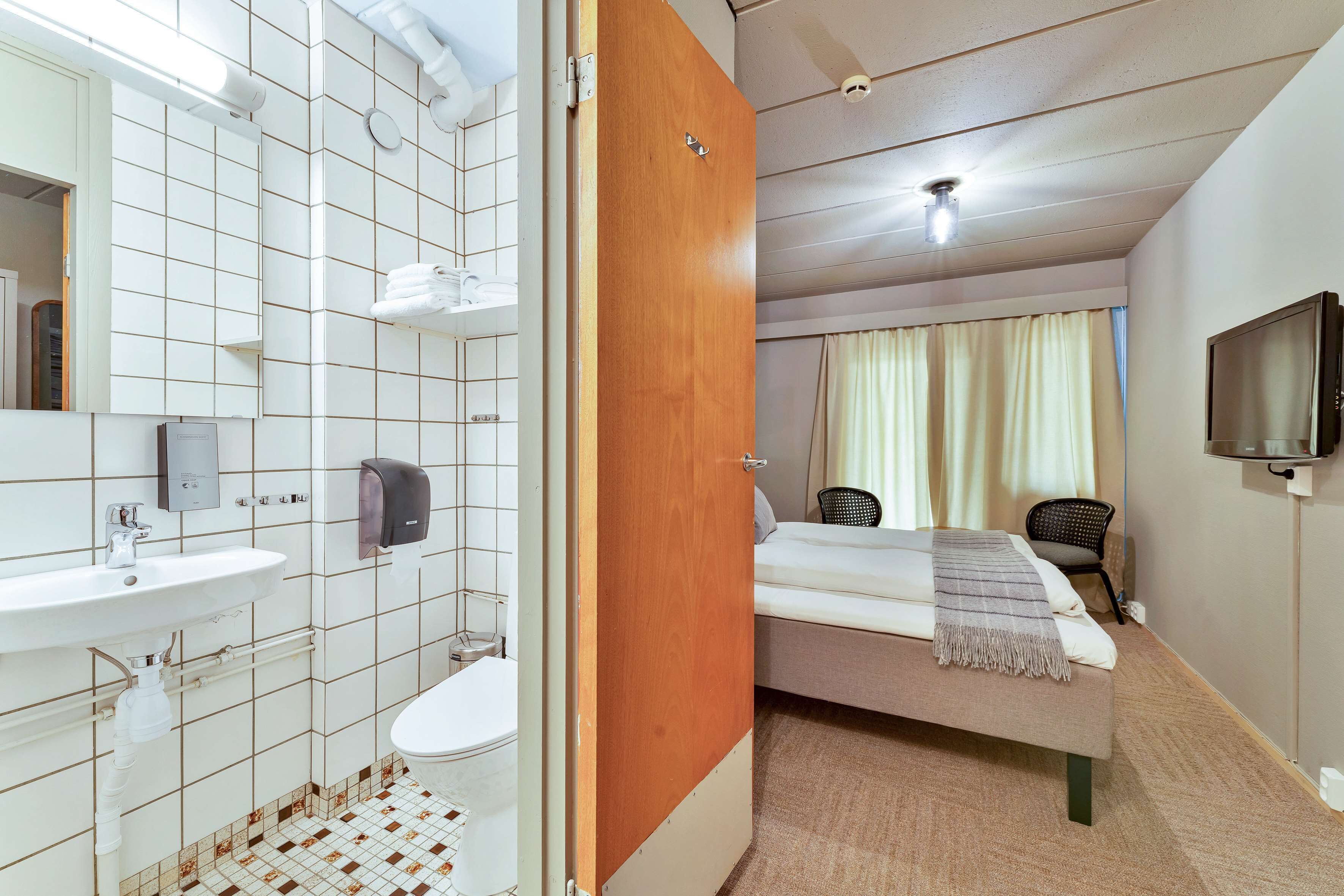 Una habitación de hotel con baño, una cama, televisión y ventana con cortinas.