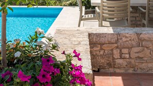 Area piscina con muro in pietra, arredi da esterno e una pergola.
