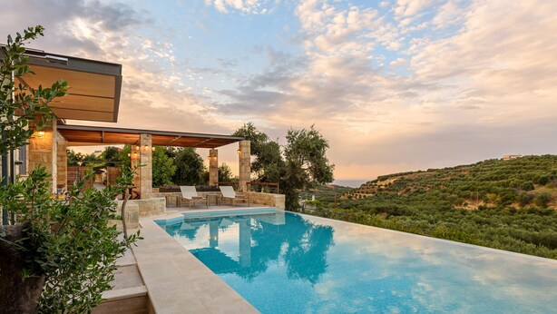 Un'area piscina moderna all'aperto con pilastri in pietra, sedie a sdraio e una pergola.
