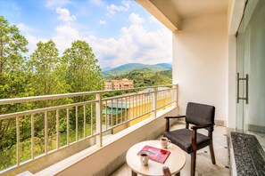 A balcony with a view of green hills and a building in the distance. There is a chair and a small table with a cup and a book. - Mewar Palace Luxury Resort & Private Pool Villas - Udaipur (Udaipur)
