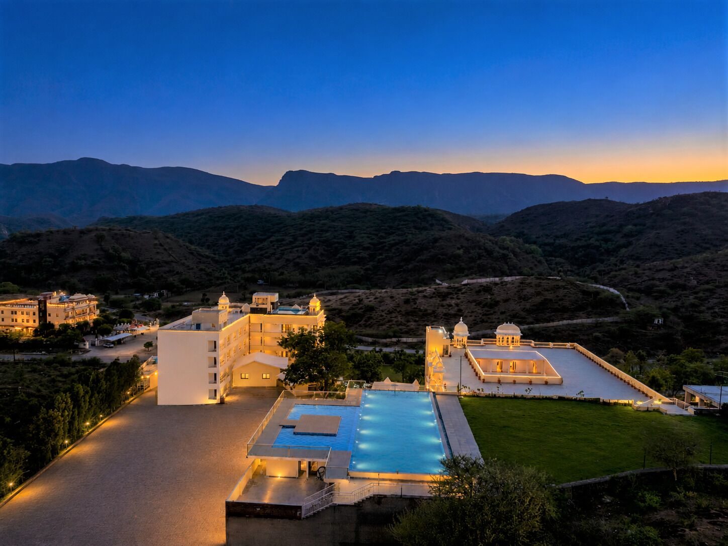 A resort with a swimming pool, multiple buildings, and a mountainous backdrop.