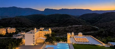 A resort with a swimming pool, multiple buildings, and a mountainous backdrop.
