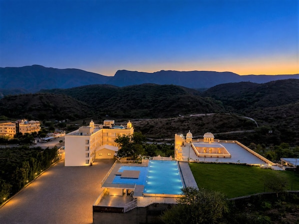 A resort with a swimming pool, multiple buildings, and a mountainous backdrop.
