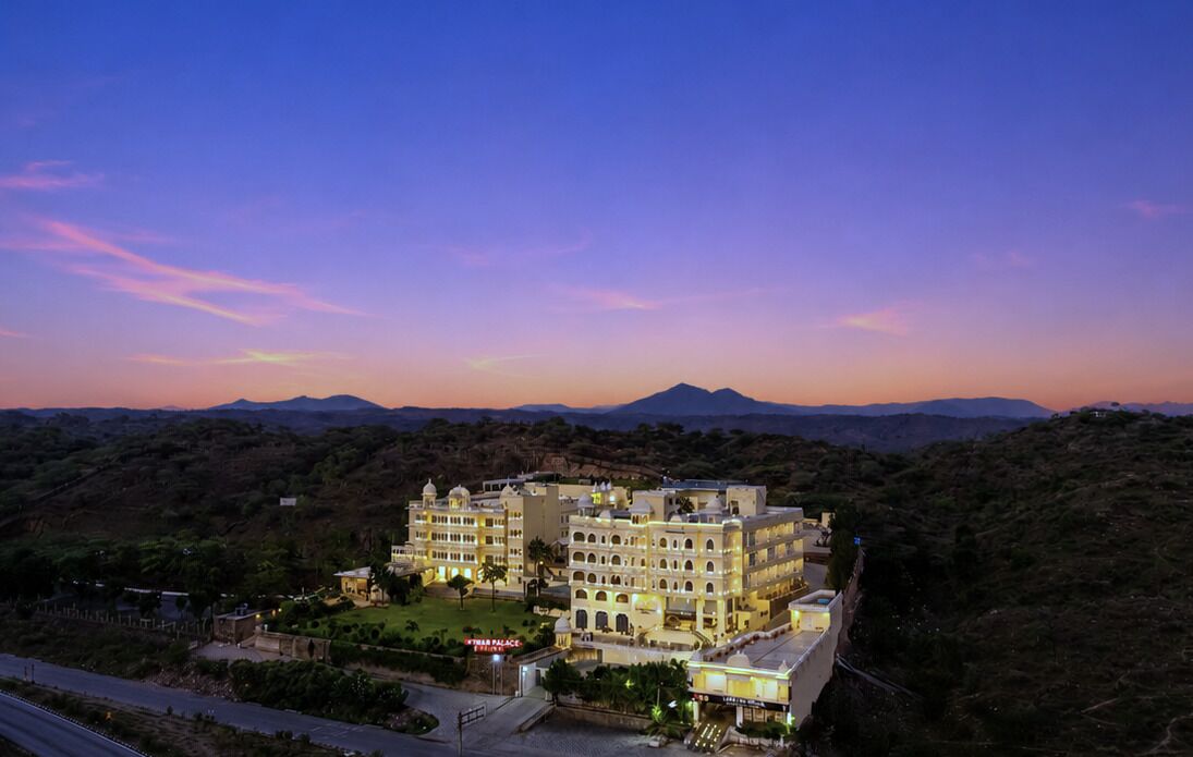 Un hotel de varios pisos con estilo arquitectónico tradicional, rodeado de abundante vegetación y colinas al fondo.
