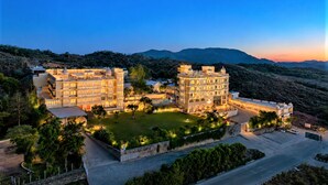 A large hotel with multiple buildings, a well-maintained lawn, and a view of the surrounding hills. - Mewar Palace Luxury Resort & Private Pool Villas - Udaipur (Udaipur)