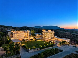 A large hotel with multiple buildings, a well-maintained lawn, and a view of the surrounding hills. - Mewar Palace Luxury Resort & Private Pool Villas - Udaipur (Udaipur)