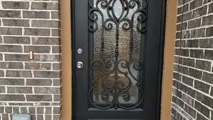Eine schwarze Metalttür mit aufwendigen Verzierungen, eingebaut in eine Ziegelwand mit weißer Grundierung.