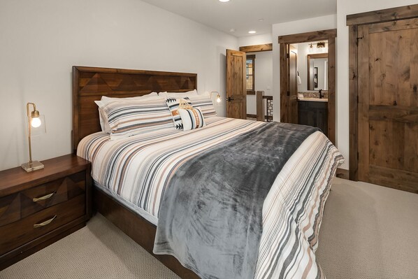 Un dormitorio con cama, cabecero de madera, mesitas de noche y un velador.