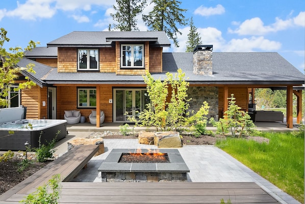 A modern two-story house with a stone chimney, a hot tub, and a fire pit in the front yard.