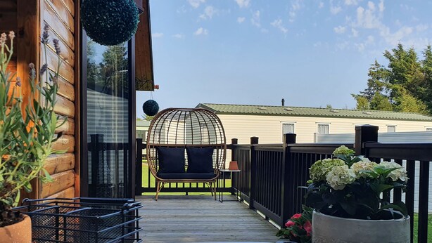A wooden deck with a wicker chair, a metal planter, and a potted plant. - The Treeline (Morpeth)