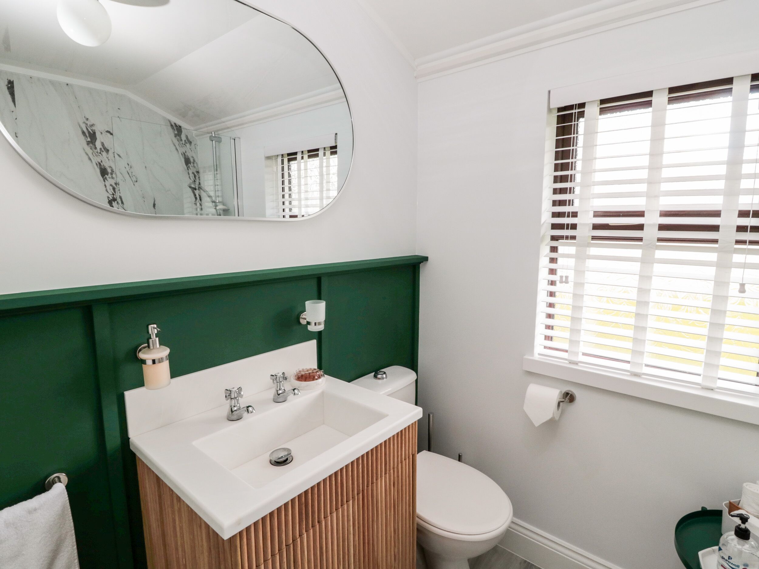 Ein Badezimmer mit weißem Waschbecken, einem grünen Waschtisch, einer Toilette und einem Fenster mit Jalousien.