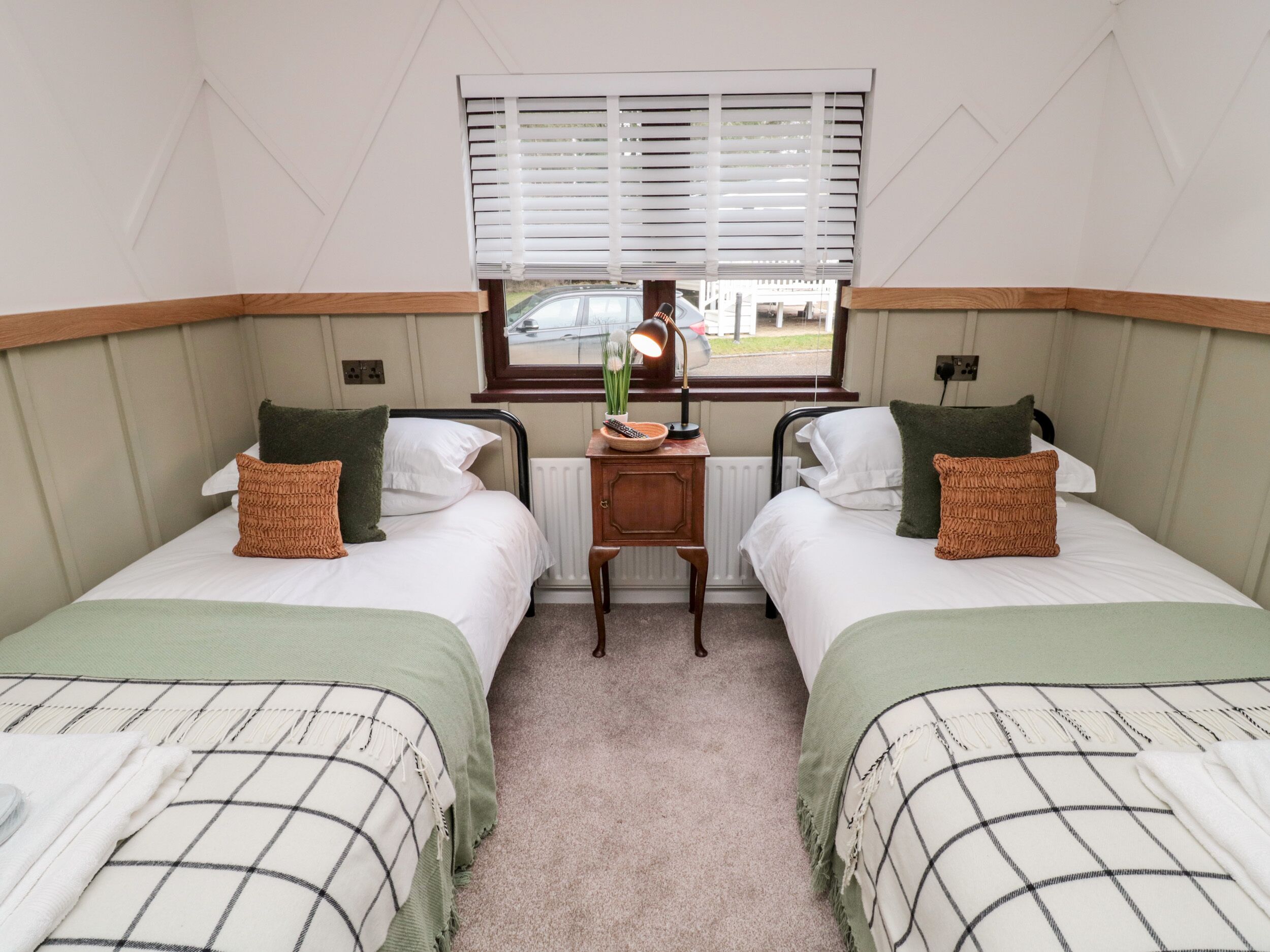 A twin room with two single beds, a small table, and a window with blinds.