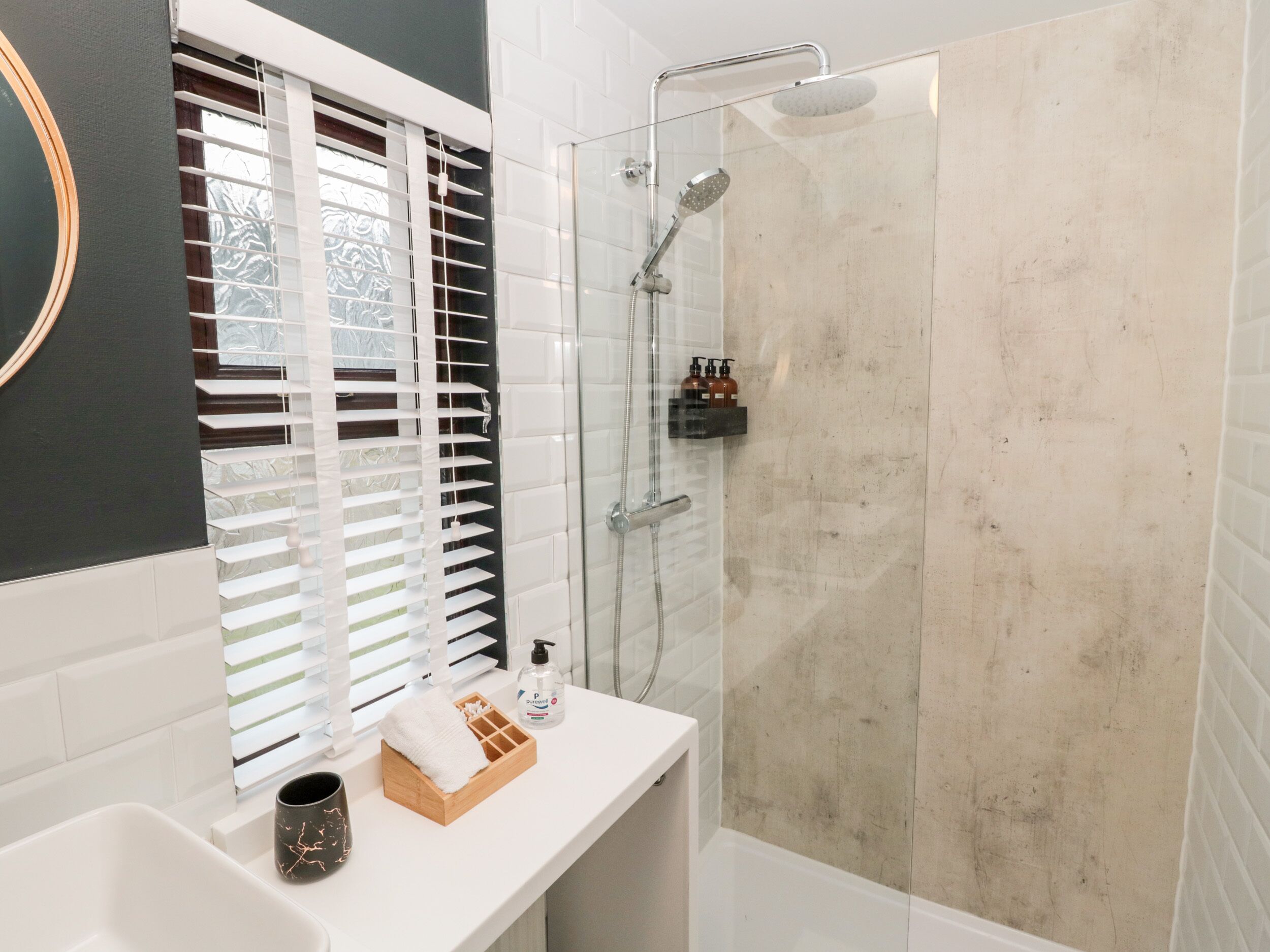 A modern bathroom with a glass-enclosed shower, a white sink, and a window with blinds.