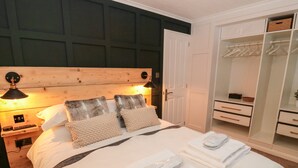 A bedroom with a large bed, a wooden headboard, a wardrobe, and a nightstand with a lamp. - The Treeline (Morpeth)