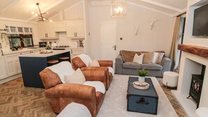 A modern living room with leather sofas, a grey sofa, and a coffee table. There is a fireplace, a television, and a kitchen in the background. - The Treeline (Morpeth)
