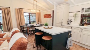 A modern kitchen with a central island, bar stools, and a dining area with a view. - The Treeline (Morpeth)