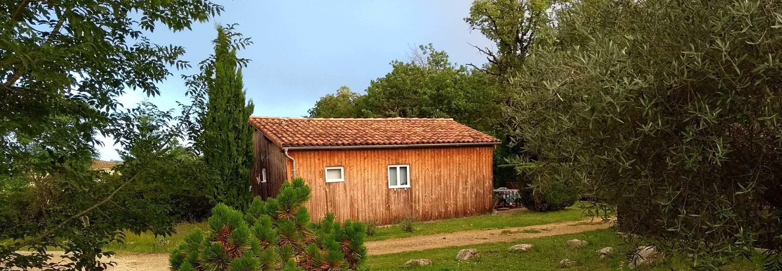 Una cabaña de madera con techo de tejas, rodeada de árboles y arbustos.