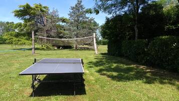 Una mesa de ping pong portátil en un espacio al aire libre con césped, con una instalación de voleibol con red al fondo.