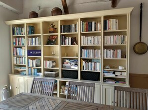 A room with a large bookshelf filled with books, a dining table with chairs, and a white cabinet.