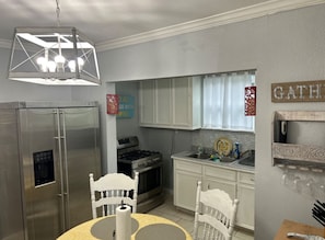 Cozinha compacta com geladeira, fogão e pia. Há uma mesa de jantar com cadeiras e um lustre.