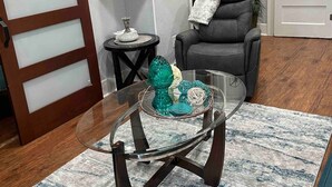 A living room with a glass coffee table, a leather armchair, a fireplace, and a door with frosted glass panels. - Location! Location! Location!  (Houston)