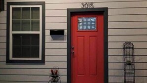 A red door with the number 3015, a window with blinds, and a small metal plant holder on the porch. - Location! Location! Location!  (Houston)